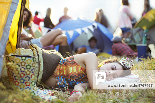 Woman with tiara sleeping in sleeping bag outside tents at music festival