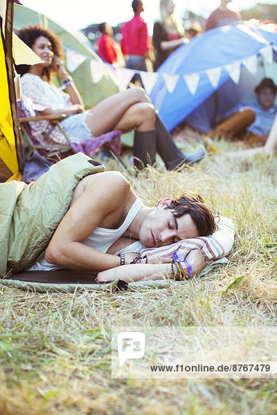 Mann im Schlafsack schläft vor den Zelten beim Musikfestival