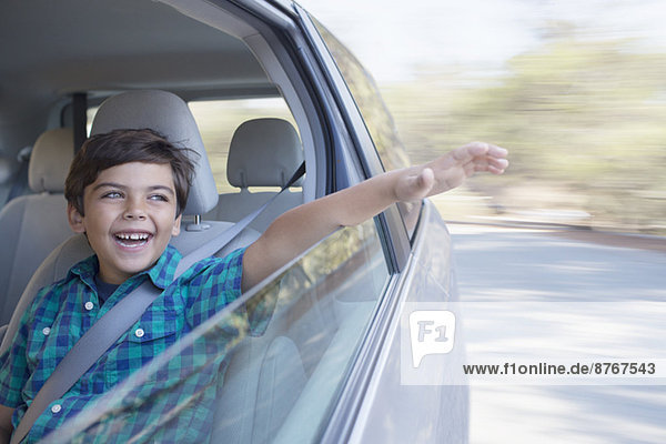 Glücklicher Junge  der die Hand aus dem Autofenster hält.