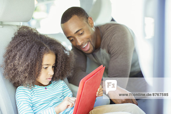 Vater und Tochter mit digitalem Tablett auf dem Rücksitz des Autos