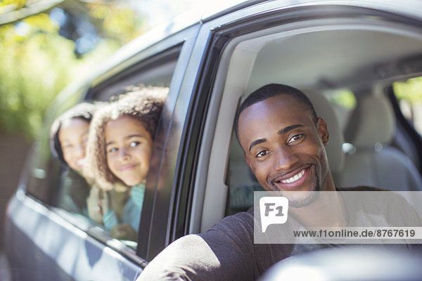 Porträt einer glücklichen Familie die sich aus den Autoscheiben lehnt.