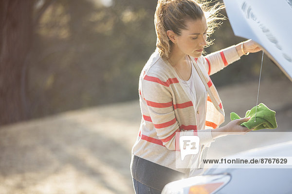 Woman checking oil under automobile hood at roadside