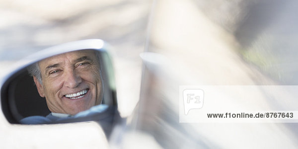 Reflektion des lächelnden Senioren im Seitenspiegel des Autos
