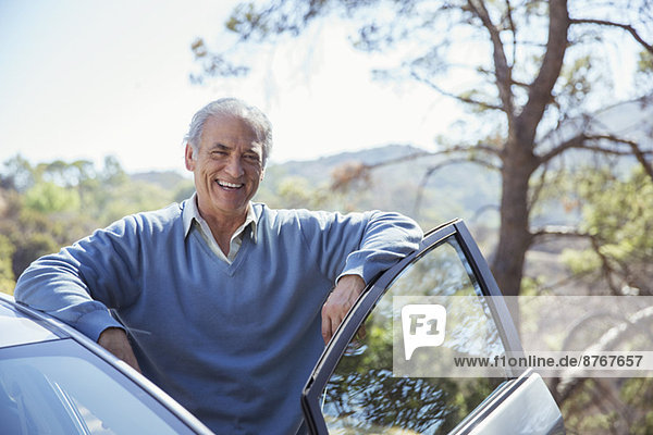 Porträt eines glücklichen älteren Mannes  der sich auf das Auto stützt.