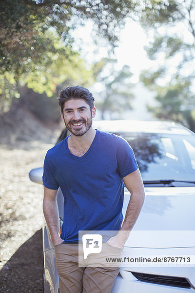 Porträt eines lächelnden Mannes  der sich auf das Auto stützt.