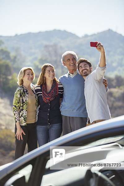 Selbstporträt der Familie mit Handy außerhalb des Autos