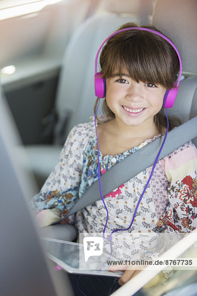 Porträt eines glücklichen Mädchens mit Kopfhörer mit digitalem Tablett auf dem Rücksitz des Autos
