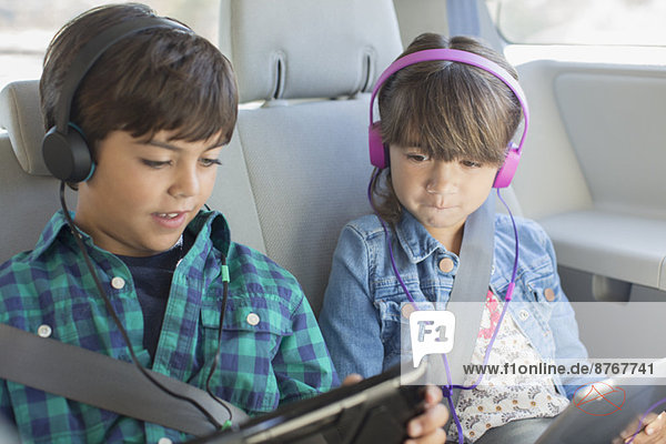 Bruder und Schwester mit Kopfhörer mit digitalen Tabletts auf dem Rücksitz des Autos