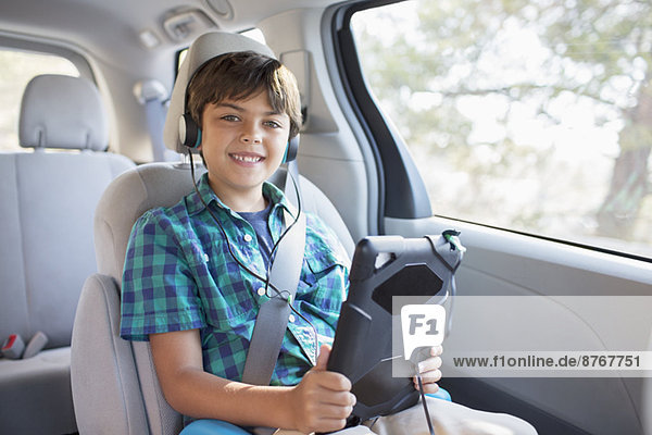 Porträt eines glücklichen Jungen mit Kopfhörer mit digitalem Tablett auf dem Rücksitz des Autos