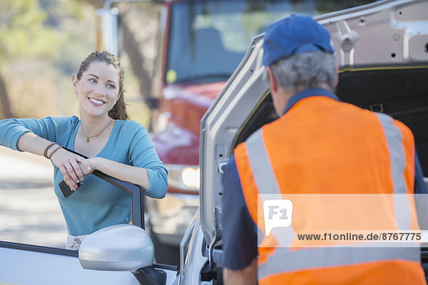 Grateful woman watching roadside mechanic fix car
