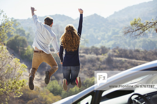 Enthusiastisches Paar  das vor Freude außerhalb des Autos springt.