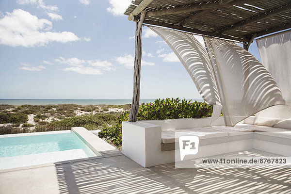 Vorhänge im Wind auf der luxuriösen Terrasse am Pool mit Blick auf den Ozean