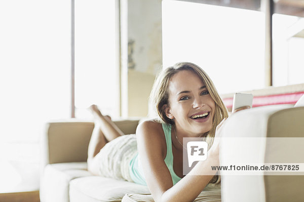 Porträt einer glücklichen Frau mit Handy auf dem Sofa