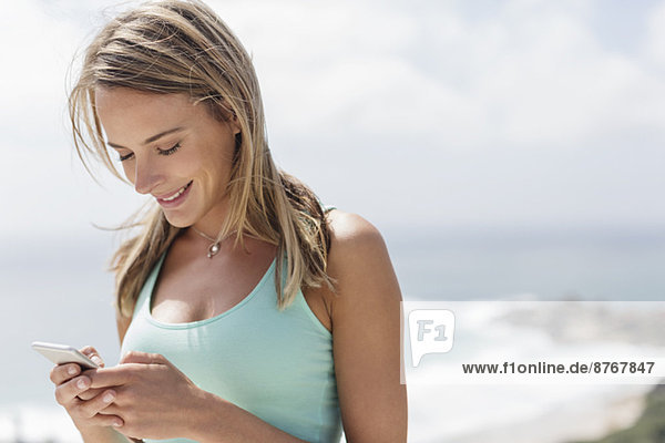 Lächelnde Frau SMS mit Handy vor dem Meer