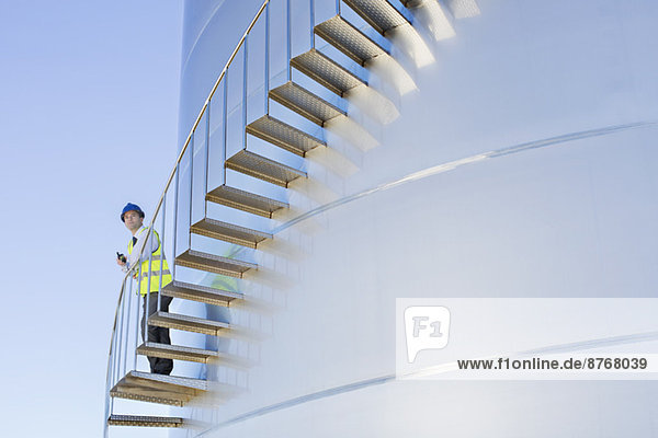 Arbeiter mit Walkie-Talkie auf einer Treppe  die sich am Silo-Lagerturm entlang schlängelt.