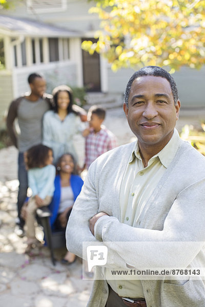Porträt eines lächelnden älteren Mannes mit Mehrgenerationen-Familie im Hintergrund