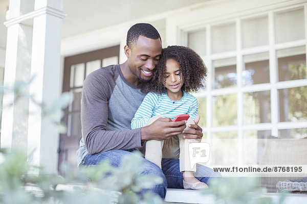 Vater und Tochter mit Handy auf der Veranda