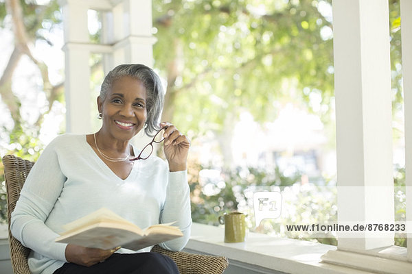 Porträt der lächelnden Seniorin beim Lesen auf der Veranda