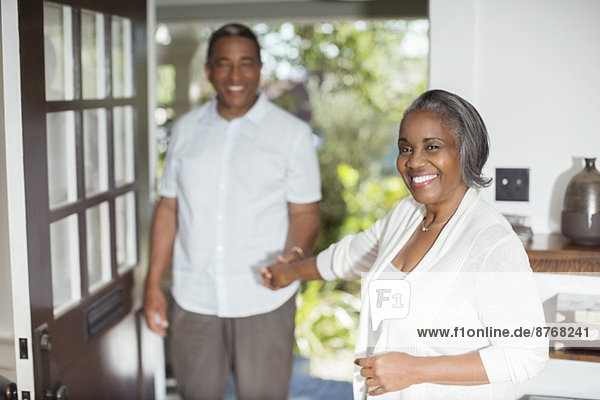 Porträt eines lächelnden Seniorenpaares  das sich an den Händen in der Tür hält.