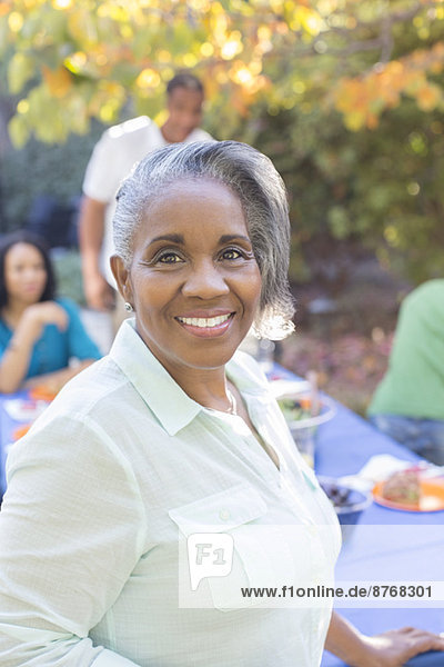 Close up portrait of smiling senior woman on patio with family in background