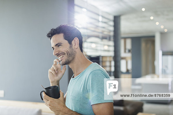 Happy man talking on cell phone and drinking coffee at home