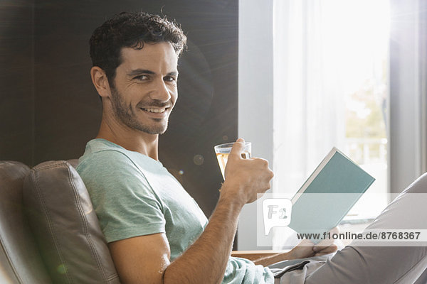 Porträt eines lächelnden Mannes  der Tee trinkt und Buch liest.