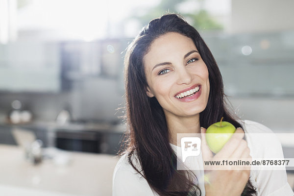 Porträt einer lächelnden Frau beim Apfelessen in der Küche