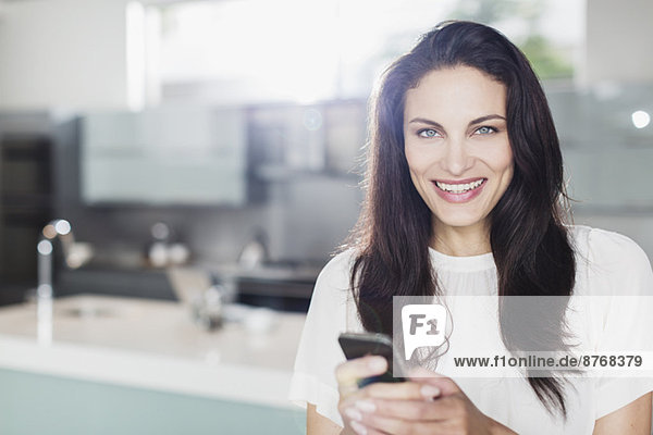 Porträt einer lächelnden Frau mit Handy in der Küche