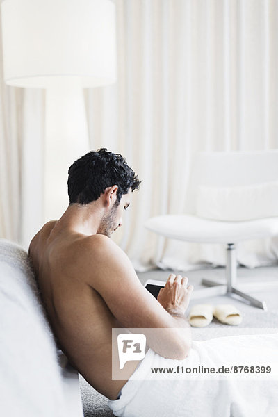 Mann im Handtuch mit digitalem Tablett im Schlafzimmer