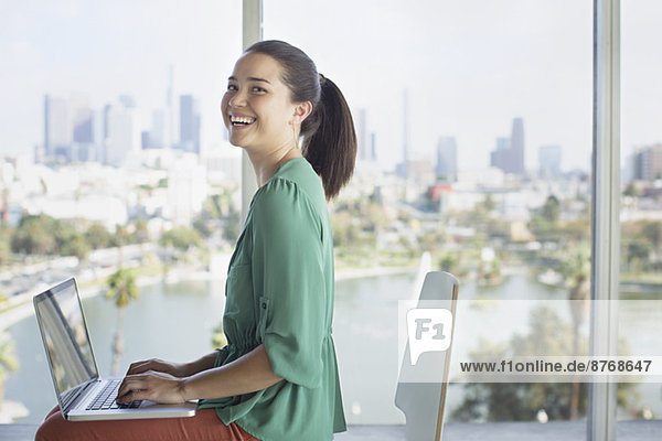 Portrait einer selbstbewussten Geschäftsfrau am Laptop in der Nähe des Fensters mit Blick auf die Stadt