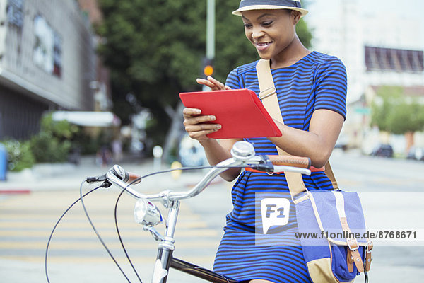 Lässige Geschäftsfrau mit digitalem Tablett auf dem Fahrrad auf der städtischen Straße