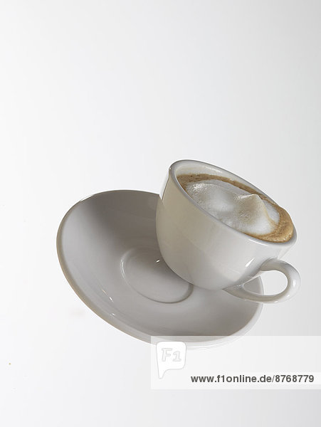Weiße Kaffeetasse mit weißem Kaffee und Untertasse vor weißem Hintergrund