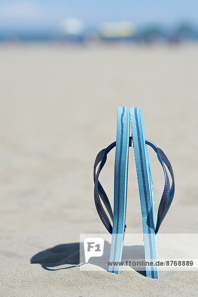 Paar hellblaue Flip-Flops im Sand stehend