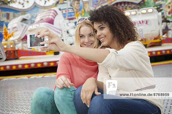 Two young women at the fairground photographing self