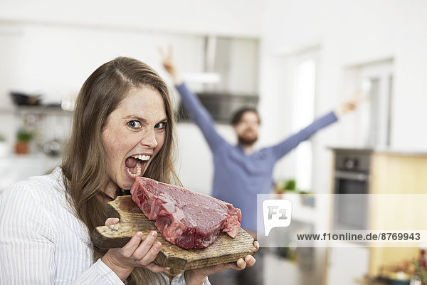 Happy young womanpretending to bite into raw steak