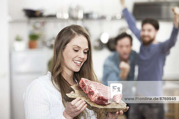 Happy young woman holding chopping board with raw steak