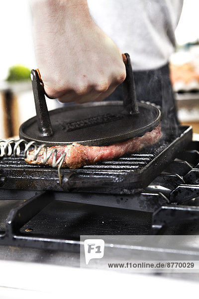 Close-up of man grilling steak in kitchen