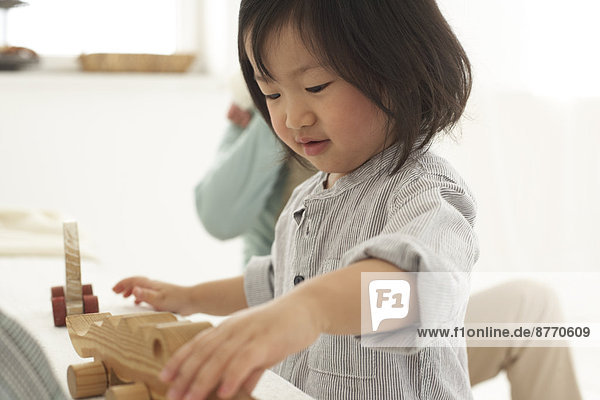 Kleines asiatisches Mädchen spielt mit ihrem Holzspielzeug