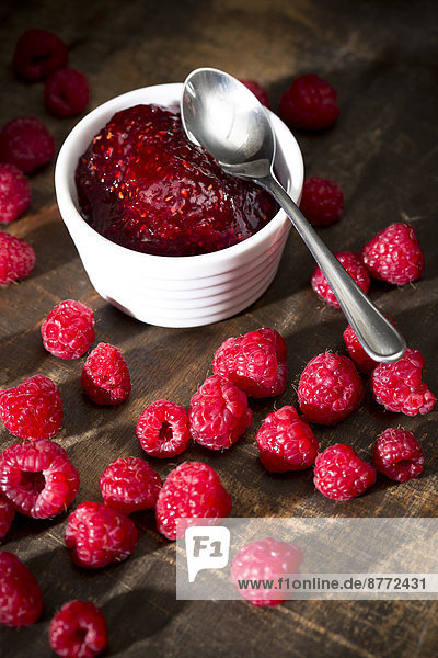 Bowl of raspberry jam  spoon and raspberries on wooden table