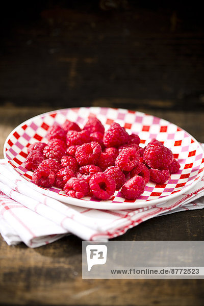 Dish of raspberries on kitchen towel and wooden table