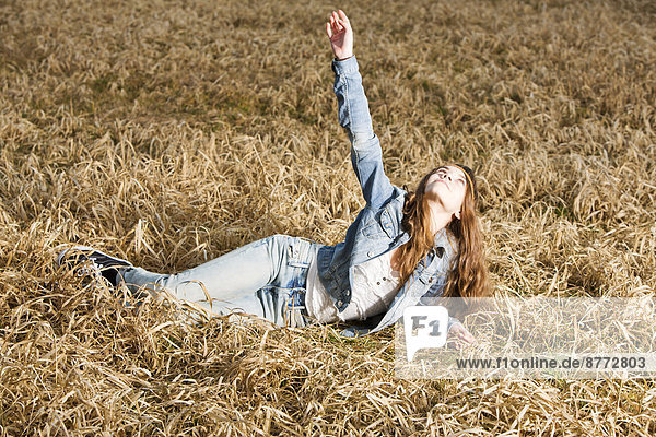 Porträt eines jungen Mädchens mit ausgestrecktem Arm auf dem Feld liegend