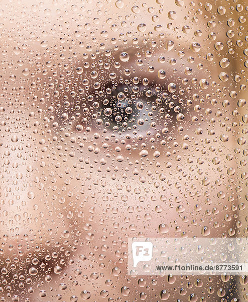 Gesicht eines Mädchens durch Glasscheibe mit Regentropfen
