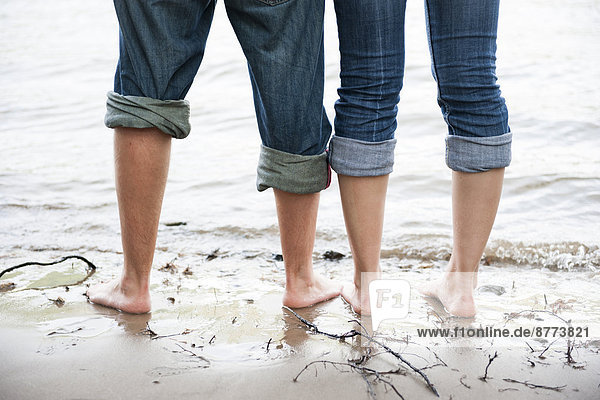Nackte Füße eines jungen Paares  das im Wasser des Rheins steht.