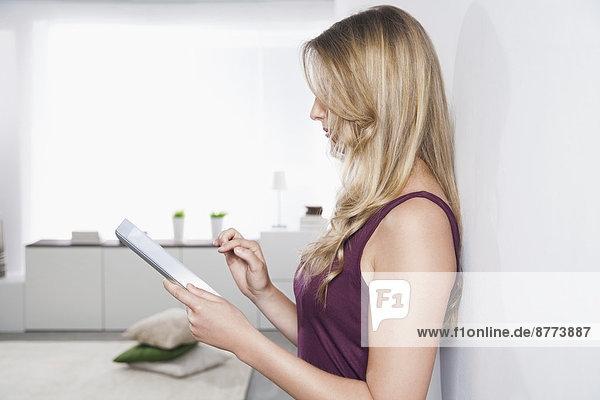 Portrait einer jungen Frau  die sich mit einem Tablet-PC an die Wand lehnt.