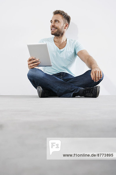 Portrait of young man sitting on floor holding tablet computer