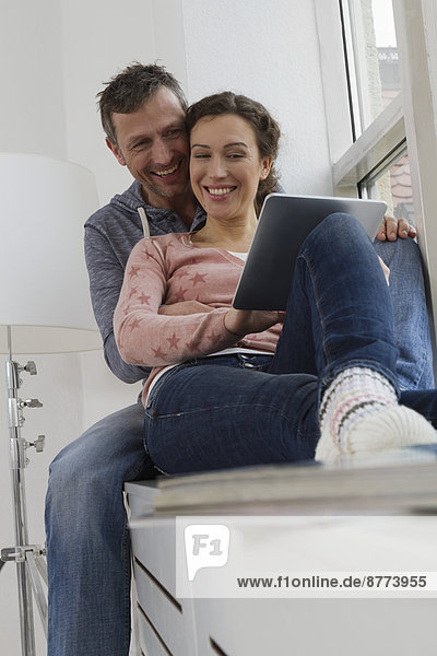 Couple sitting on windowsill using tablet computer