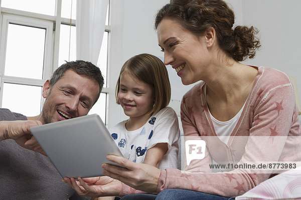 Mutter,  Vater und Tochter auf Couch mit Tablet-Computer