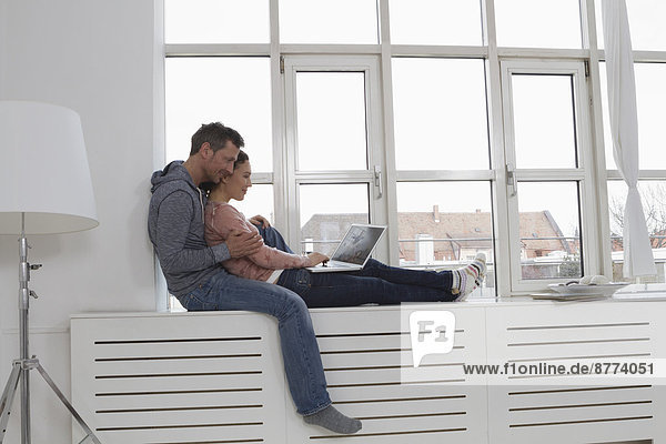 Couple sitting on windowsill using laptop