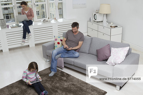 Mother  father and daughter using portable devices in living room
