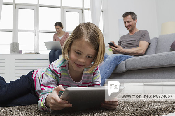 Mother  father and daughter using portable devices in living room